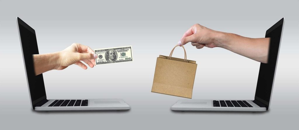 ecommerce - two laptops - two hands - a paper bag and 100 dollar bill - exchange