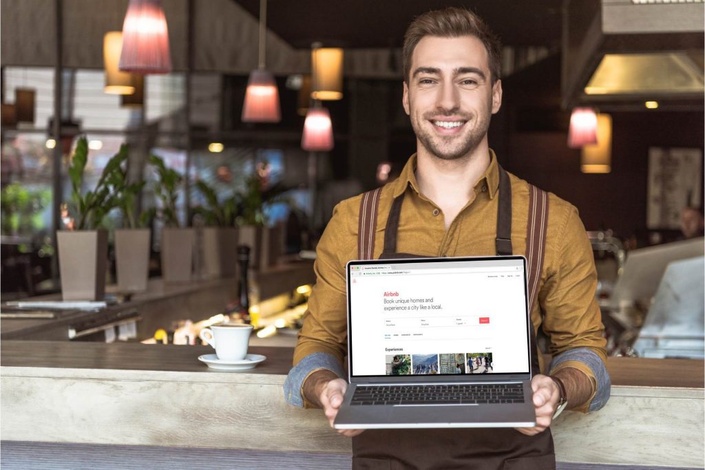 waiter holding laptop with airbnb website on screen in cafe
