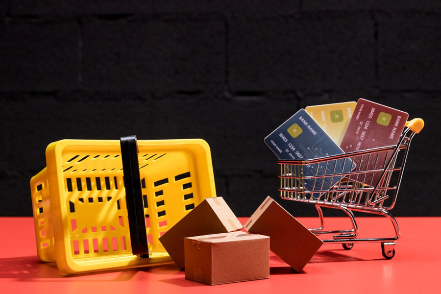 A picture of a small shopping cart with credit cards in it, and a shopping basket and packages next to it.