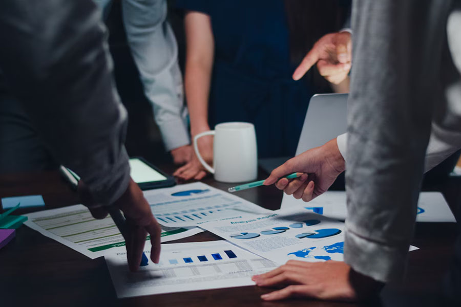 A zoomed-in photo of a desk with papers and people around it, having an important meeting. 